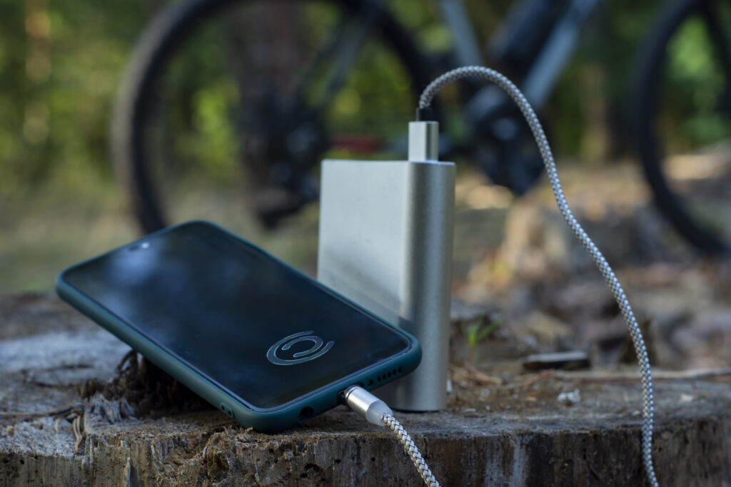 Power bank charges a smartphone in the forest on the background of a bicycle.