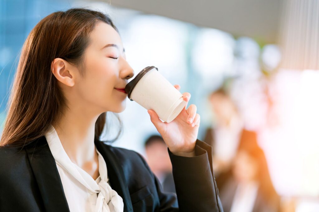 Close up smart attractive asian business female smile hand hold hot drink with modern office background